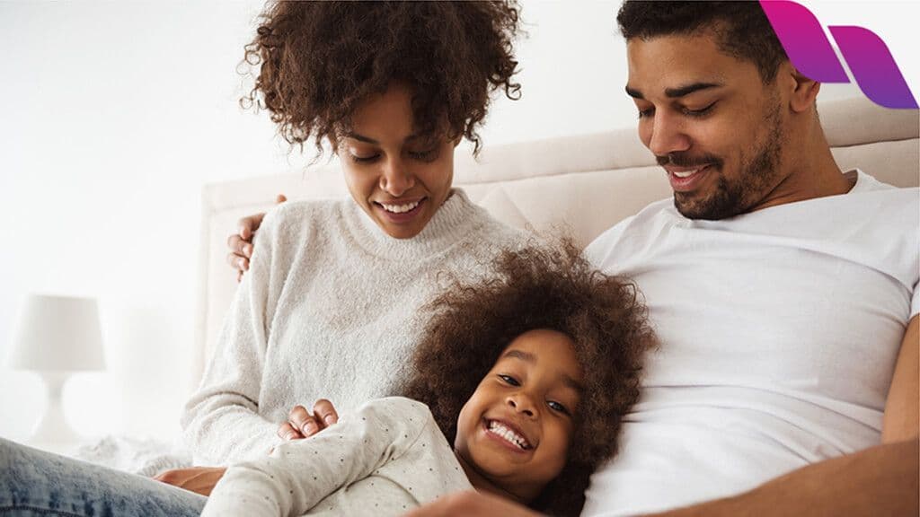 man, woman, and child laying in bed smiling at eachother