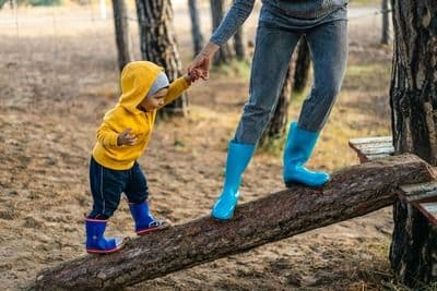 Kid with their parent walking on a tree log