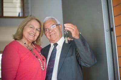 A man and woman standing by the door of their home with keys in their hand